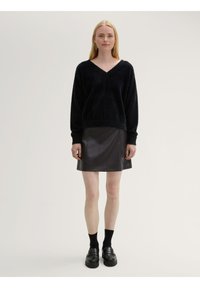 Suéter negro, esponjoso, con cuello en v y mangas largas, combinado con una mini falda de cuero ecológico oscura. Mocasines negros y calcetas altas completan el look.