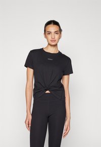 Zwart geknoopt T-shirt met korte mouwen en een ronde hals, featuring een klein logo. Gecombineerd met zwarte leggings, wat een monochrome look creëert.