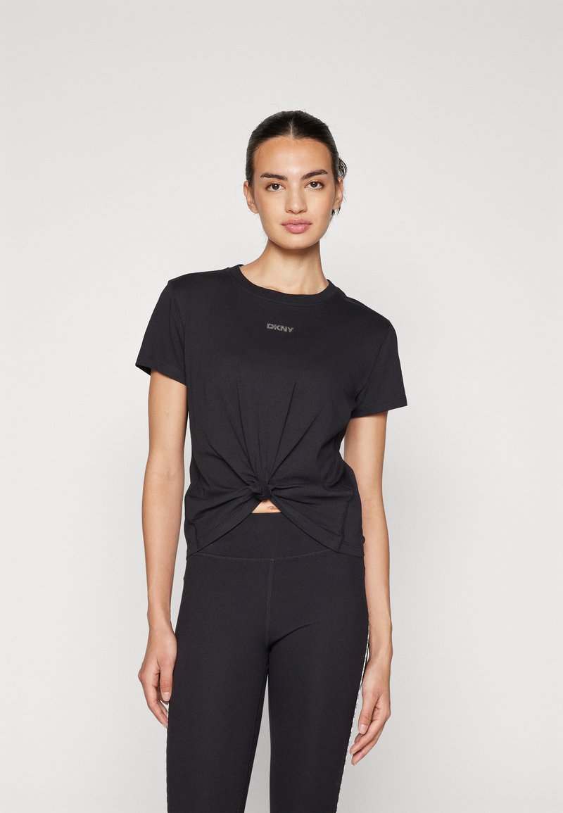 Zwart geknoopt T-shirt met korte mouwen en een ronde hals, featuring een klein logo. Gecombineerd met zwarte leggings, wat een monochrome look creëert.