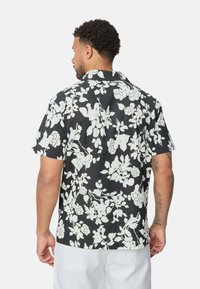 Chemise à manches courtes en tissu noir avec de grands motifs floraux blancs, un col classique et une coupe décontractée, avec un ourlet droit.