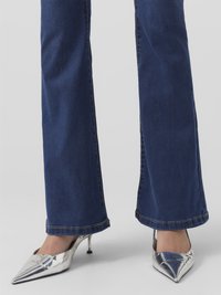 Sinised laiematest pahkluude denimid, millel on kulunud serv, koos metallik hõbedaste teravate varvastega kontsadega, millel on õhuke konts. Lähedalt vaade jalgadele ja alumistele jalgadele.