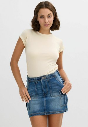 Camiseta de manga corta beige combinada con una mini falda de denim que cuenta con dos bolsillos frontales y un acabado de lavado claro.