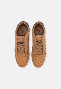 Sneakers in pelle marrone con punta perforata, lacci beige e dettagli blu sulla linguetta e sui lati. Suole in gomma piatta.