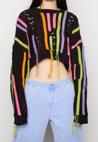 Pull court au crochet en noir avec des rayures verticales vives en rose, orange, vert et violet. Des trous et des accents de franges ajoutent de la texture.