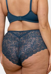 Bikini en dentelle de bleu profond avec un motif floral, présentant des bords festonnés et une finition en tissu lisse. Les bretelles sont ajustables.
