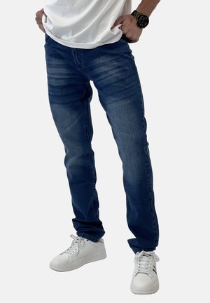 Jeans in denim blu scuro con una vestibilità slim, leggere sfumature e tasche frontali, abbinati a sneakers bianche e una maglietta bianca semplice.