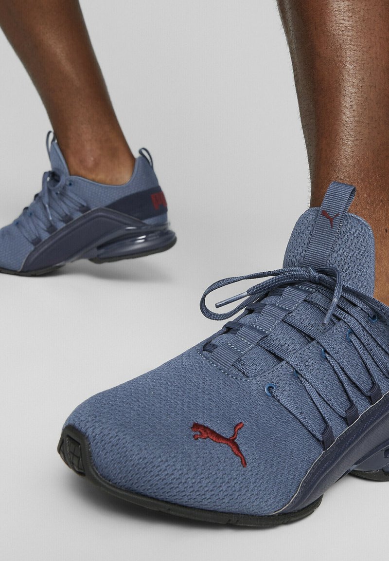 Scarpe da ginnastica blu con tomaia in rete e suola in gomma. Presentano un design con lacci, linguetta imbottita e logo Puma rosso sul lato.