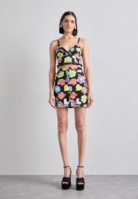Čierny kvetinový crop top s nastaviteľnými ramienkami a pom-pom ozdobou, kombinovaný s zodpovedajúcou sukňou s vysokým pásom, na ktorej sú veľké, živé kvety.