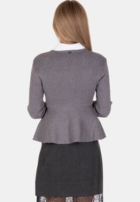 Maglione peplum grigio a coste con maniche lunghe, dotato di un colletto bianco e un bottone decorativo sul retro. Abbinato a una gonna a matita scura.
