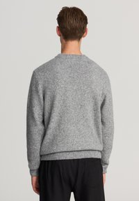 Maglione grigio a maglia con colletto rotondo classico, polsini e orlo a coste. Texture morbida, vestibilità leggermente ampia e senza motivi o dettagli visibili.