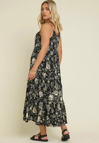 Svart blommig maxi-klänning med spagettiband; har vita och beige botaniska mönster samt en lager-på-lager fåll. Sandaler med en spänne-detalj.