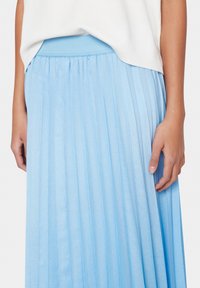 Hame maksimaali vaaleansinisestä kankaasta, jossa on sileä pinta ja joustava vyötärö. Läheltä otettu kuva, joka korostaa pystysuoria poimuja.