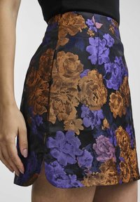 Schwarzer, floraler Minirock mit strukturierten, metallischen Blumen in Bronze und Lila. Hat einen Seitenschlitz und ein körperbetontes Design.