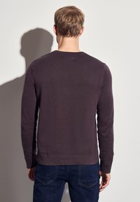 Mörklila l�ångärmad tröja med rundad halsringning, ribbade mudd och nederkant. Slät, texturerad tyg som bärs med blå jeans.