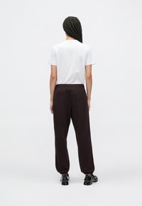 Λευκό κοντομάνικο μπλουζάκι και καφέ σκούρο, φαρδιά φούτερ παντελόνια με ελαστική μέση. Φοράει μαύρα γυαλιστερά παπούτσια με πάτο πλατφόρμα.