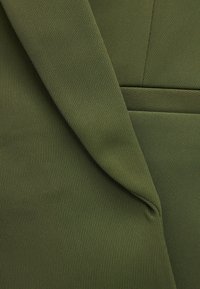 Gros plan sur un tissu côtelé vert olive plié avec des coutures visibles et des détails de texture.