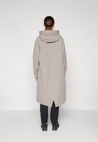 Cappotto lungo di un grigio chiaro, con cappuccio, caratterizzato da un taglio dritto e uno spacco posteriore. Texture liscia, progettato per una vestibilità casual, con un branding discreto.