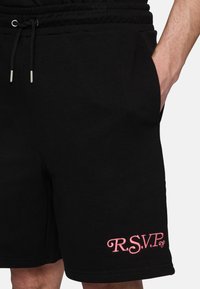 Pantaloni corti neri in cotone con vita regolabile, tasche laterali e dettagli ricamati in rosa "R.S.V.P." sul lato inferiore sinistro.