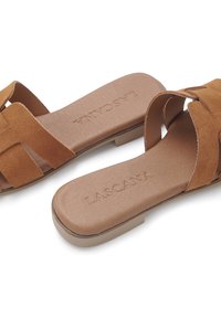 Brown suede slide sandals with crisscross straps and a flat, tan outsole. Features a cushioned footbed with embossed "LASCANA" logo.