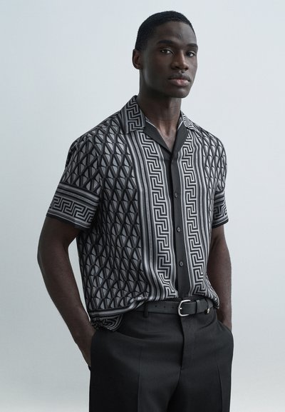 Camicia a maniche corte con motivo geometrico bianco e nero, colletto con bottoni, abbinata a pantaloni neri sartoriali.