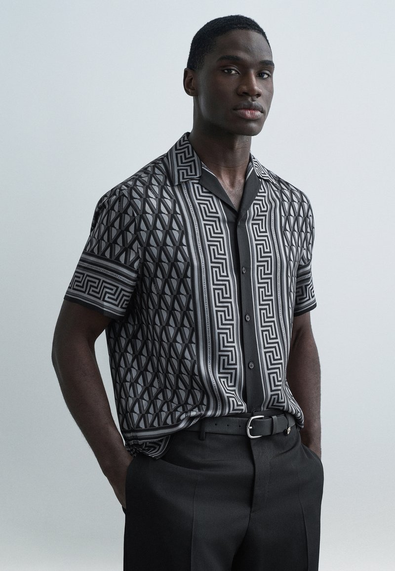 Πουκάμισο με κοντό μανίκι που φέρει γεωμετρικό α�σπρόμαυρο σχέδιο, με γιακά και κουμπιά, συνδυασμένο με καλοραμμένο μαύρο παντελόνι.