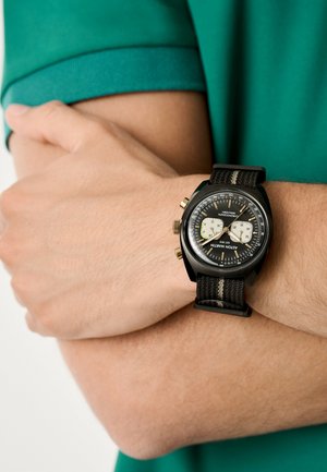 Orologio cronografo nero con cinturino in tessuto testurizzato e accenti dorati, dotato di un quadrante nero con sottoquadranti bianchi e una scala tachimetrica.