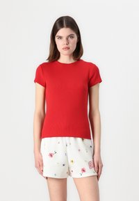Rød ribbet kortærmet t-shirt med rund halsudskæring, parret med hvide shorts med et farverigt blomstermønster og broderede detaljer.