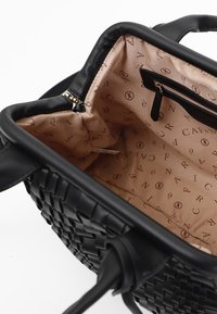 Borsa intrecciata nera con toppa in pelle liscia. L'interno presenta una fodera beige con un logo a motivo sottile e una tasca con cerniera.