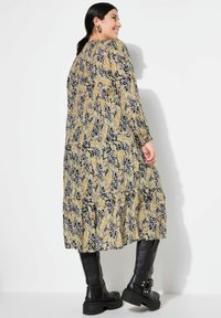 Robe à motifs floraux dans des teintes de bleu marine, jaune et blanc, présentant des manches longues, un design en couches, et assortie à des bottes noires jusqu'aux genoux.