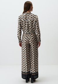 Gemusteter Jumpsuit aus leichtem Stoff; mit geometrischen Formen in Beige, Marineblau und Braun. Lange Ärmel und weiter Beinschnitt.