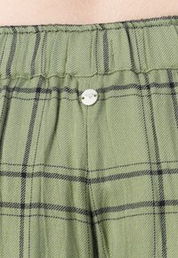 Green and black plaid fabric with gathered waistband and a small round silver button sewn at the center.
