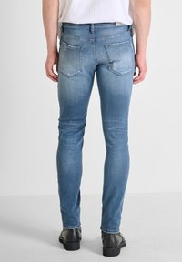 Vaqueros de mezclilla azul claro con un corte slim, que cuentan con dos bolsillos traseros, un ligero desgaste y costuras de contraste. Llevados con zapatos negros.