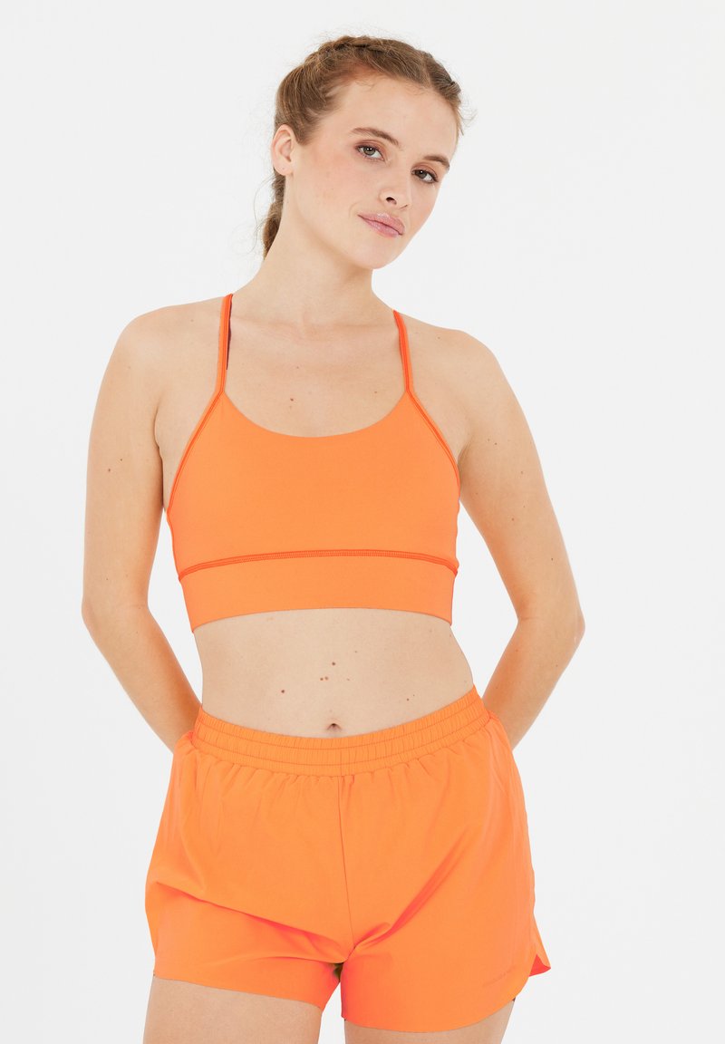Orange sportbh med tunna axelband och en åtsittande design, parat med orange shorts med elastisk midja som har en lös passform och en mjuk textur.