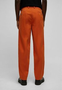 Oranje wijde broek met achterzakken en metalen knopen, met een gladde katoenstructuur en een relaxte pasvorm. Draag met zwarte schoenen.
