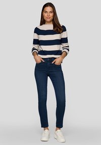 Marineblauer und cremefarbener gestreifter Pullover mit rundem Ausschnitt, kombiniert mit dunkelblauen Skinny-Jeans und weißen Turnschuhen. Glatte Textur und lässige Passform.