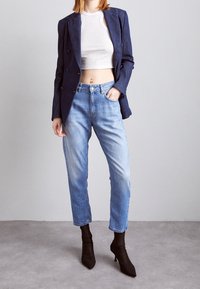 Blazer azul marino de doble botonadura sobre un top corto blanco, combinado con vaqueros de pierna recta en azul claro y tacones negros de punta fina.