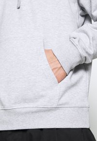 Grå sweatshirt med en frontlomme (kangaroo pocket), ribbede manchetter og kant. Stoffet ser blødt og let tekstureret ud, velegnet til afslappet brug.