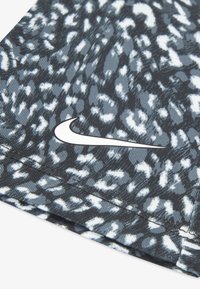 Крупен план на черно-бяла плат с леопардов принт и бяло лого Nike swoosh, отпечатано върху него.