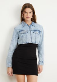 Lett denimjakke i lyse vask med lange ermer, to brystlommer og glidelås, kombinert med en tettsittende svart kjole.