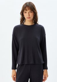 Donker geribbelde longsleeve met een ronde halslijn. Zachte stof, relaxte pasvorm, iets langere zoom en textuurafwerking. Gecombineerd met bijpassende broek.