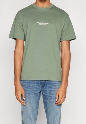 Grøn bomuld T-shirt med rund hals, korte ærmer og hvid tekst med "Originals Studio" tværs over brystet. Casual pasform.