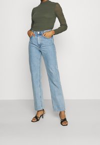 Top a maniche lunghe ribbed verde oliva, jeans a vita alta azzurri chiari a gamba larga e sandali neri con tacco alto e cinturini.