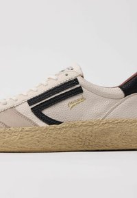 Sneaker con tomaia in pelle crema, dettagli neri, superficie testurizzata, lacci bianchi e suola in gomma naturale testurizzata. Dettaglio del logo dorato presente.