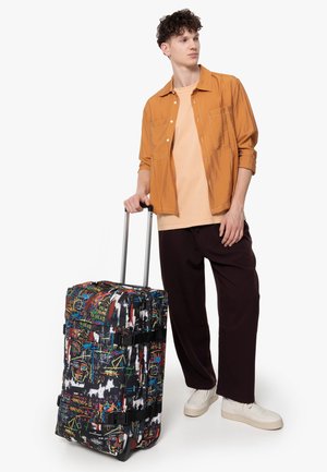 Rolling suitcase with a multicolored graffiti design, black fabric, adjustable straps, and a sturdy handle; features a zip closure on top.
