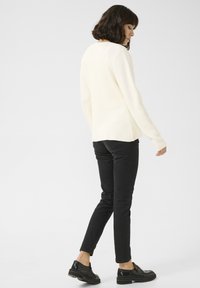 Pull crème avec une finition texturée, manches longues et coupe décontractée, associé à un jean slim noir et des mocassins noirs.
