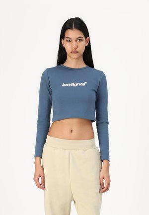 Light blue cropped long-sleeve top with white "lowlights" text; paired with beige elastic-waist sweatpants. Smooth fabric texture.