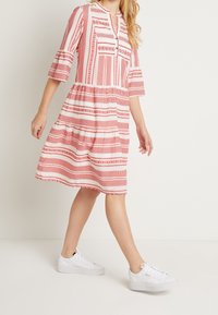 Rotes und weißes gemustertes Kleid mit Dreiviertelärmeln, Rundhalsausschnitt und gerafftem Taillenbereich, kombiniert mit weißen Sneakern.