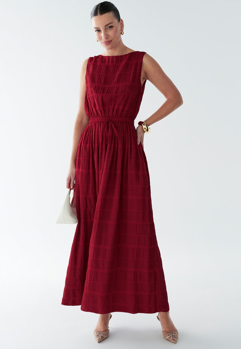Rød maxikjole med en struktureret overdel, smocket talje og tekstureret krøllede stof. Har et ærmeløst design og elegant, flydende nederdel.