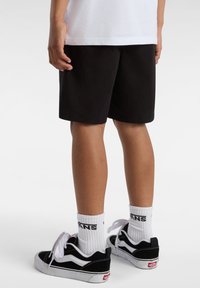 Shorts neri realizzati in tessuto morbido, di lunghezza al ginocchio con un taglio semplice, abbinati a sneakers bianche e nere e calze bianche con un logo.