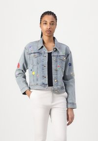 Ljusblå denimjacka med blommönster i röd, lila och gul; har knäppning med knappar, bröstfickor och kortad design.
